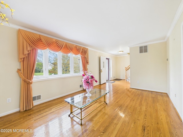 living area featuring baseboards, visible vents, ornamental molding, and light wood-style floors