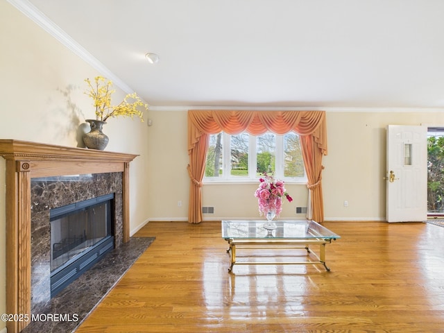 living area with wood finished floors, ornamental molding, a high end fireplace, baseboards, and visible vents