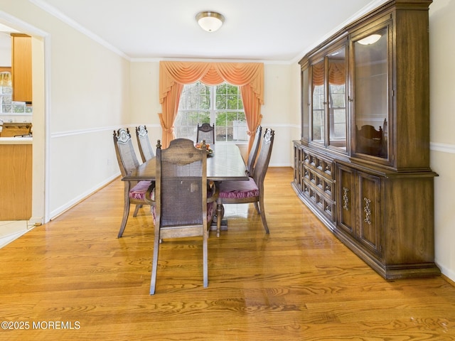 dining space with light wood-type flooring, ornamental molding, and baseboards