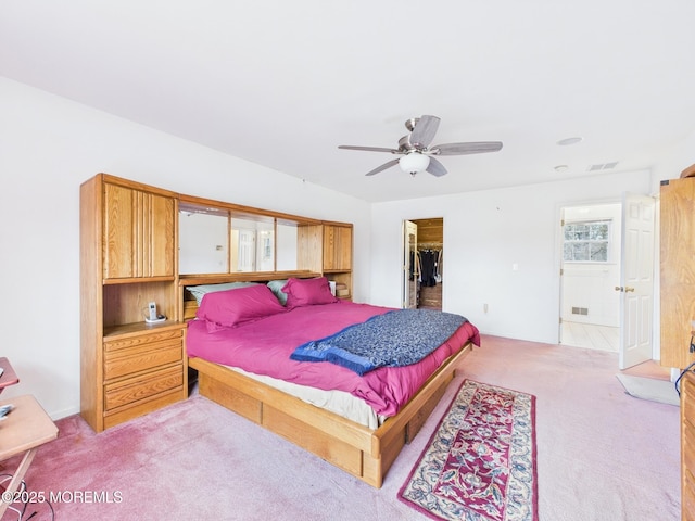 bedroom with a walk in closet, a ceiling fan, visible vents, and light carpet