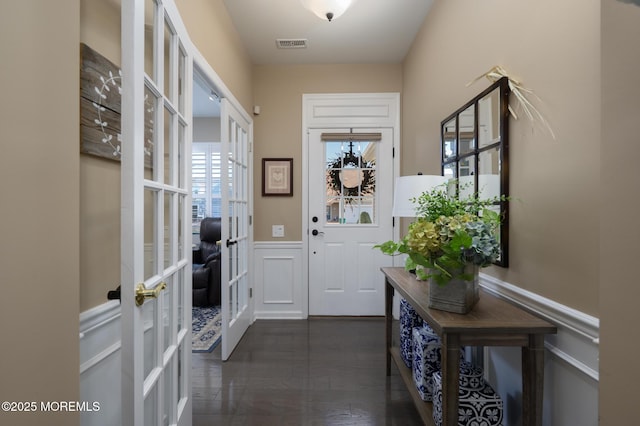 doorway to outside featuring french doors, wainscoting, a decorative wall, visible vents, and dark wood-style flooring