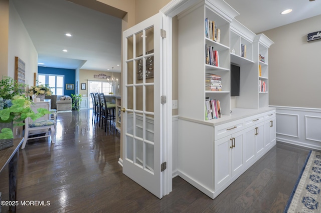 corridor with a wainscoted wall, recessed lighting, a decorative wall, and dark wood-style flooring