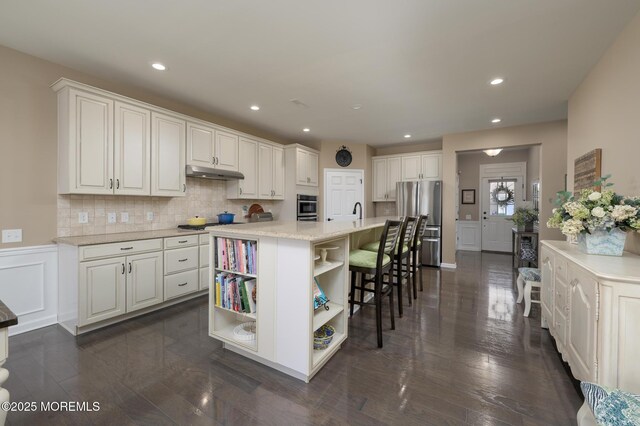 kitchen featuring open shelves, tasteful backsplash, under cabinet range hood, a decorative wall, and stainless steel appliances
