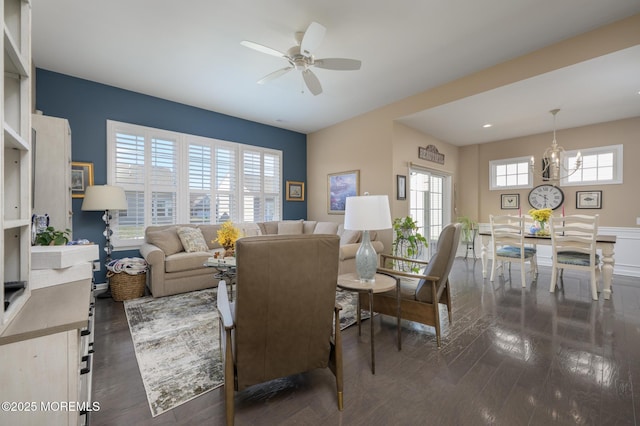 living area featuring dark wood-style floors, a healthy amount of sunlight, and ceiling fan with notable chandelier