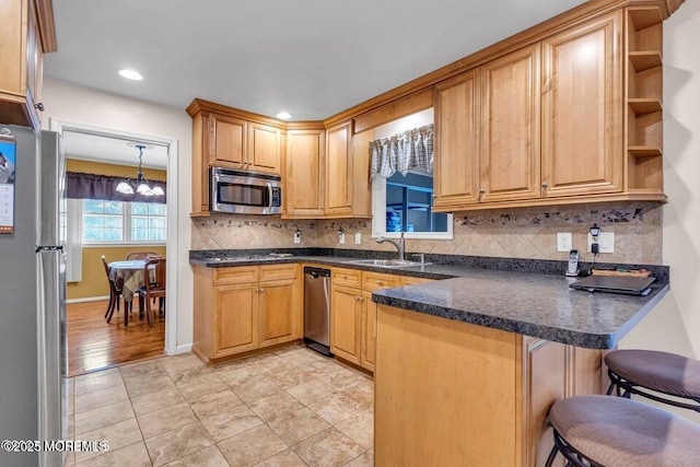 kitchen featuring a peninsula, a kitchen bar, stainless steel appliances, tasteful backsplash, and a sink