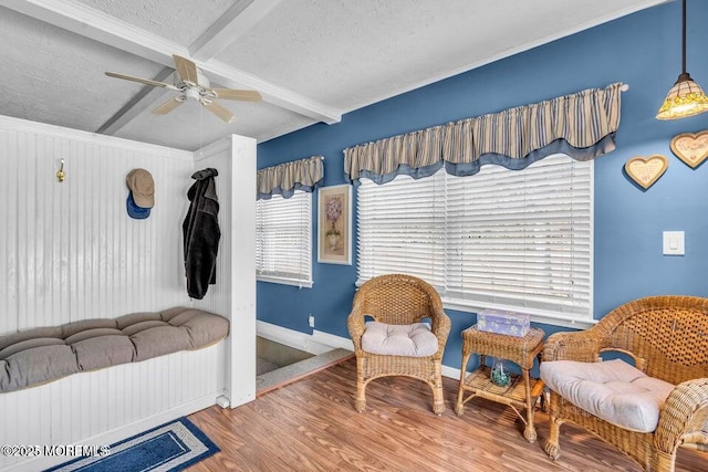 sitting room with a textured ceiling, beamed ceiling, baseboards, wood finished floors, and a ceiling fan