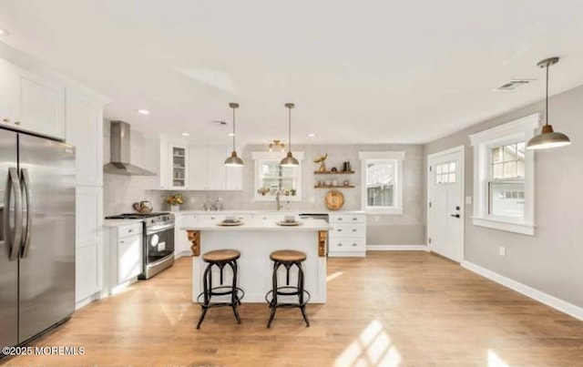 kitchen featuring white cabinetry, light countertops, a kitchen bar, wall chimney range hood, and appliances with stainless steel finishes