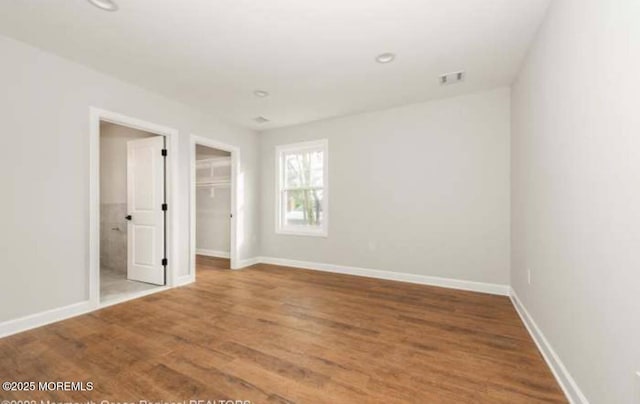 unfurnished bedroom with baseboards, visible vents, wood finished floors, and a spacious closet