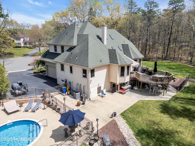 rear view of property featuring a wooden deck, a yard, a chimney, roof with shingles, and fence