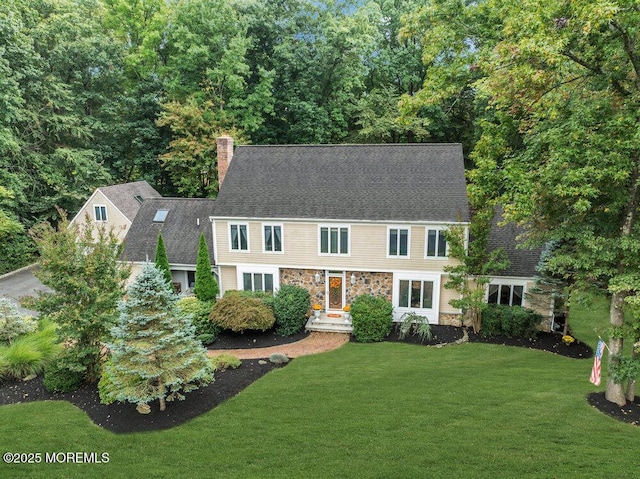 view of front facade featuring a chimney, a front yard, stone siding, and roof with shingles