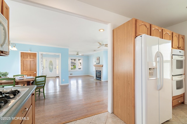 kitchen with white appliances, a fireplace with flush hearth, crown molding, light tile patterned floors, and a ceiling fan