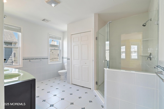 full bath with tile walls, a shower stall, double vanity, and toilet