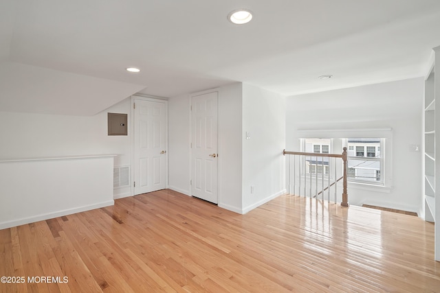 additional living space with wood finished floors, baseboards, recessed lighting, and electric panel