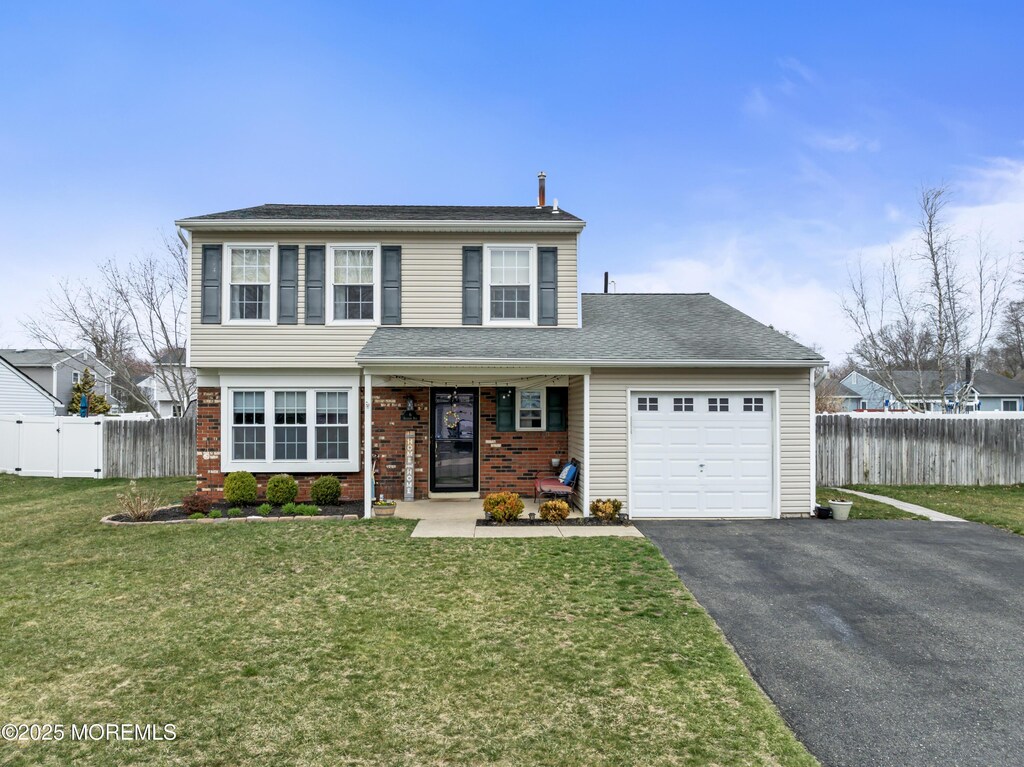 view of front of home featuring driveway, fence, brick siding, a front lawn, and a garage