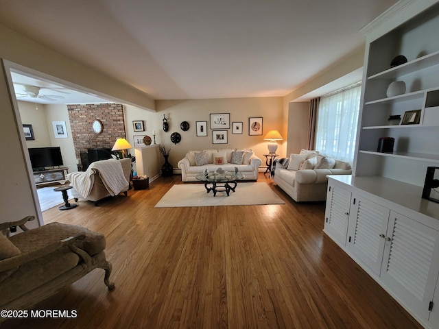 living area featuring a ceiling fan, dark wood-style flooring, and a brick fireplace