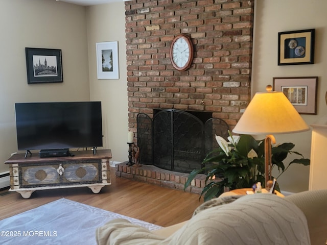living room with a brick fireplace, wood finished floors, and baseboard heating