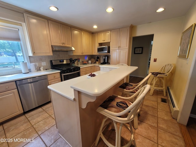 kitchen with appliances with stainless steel finishes, light countertops, a center island, tasteful backsplash, and under cabinet range hood