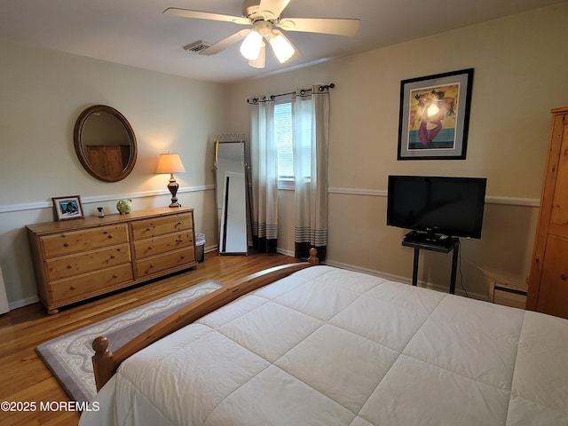 bedroom with visible vents, a ceiling fan, a baseboard heating unit, and wood finished floors