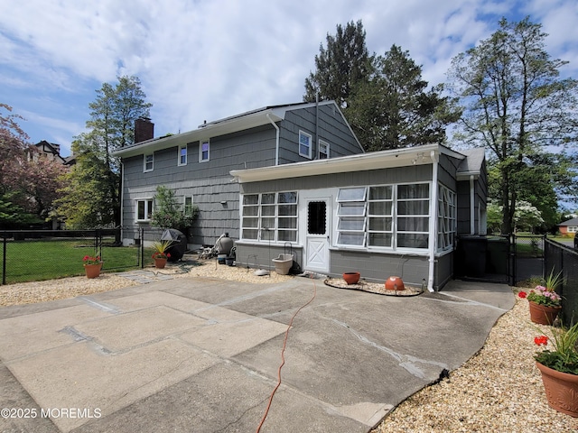back of house with fence, a sunroom, a gate, a chimney, and a patio