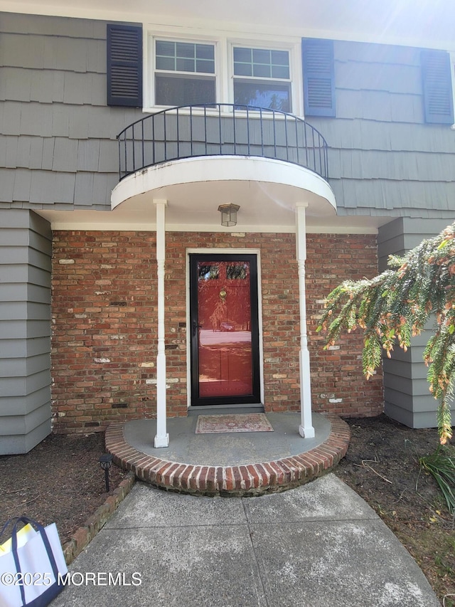doorway to property with brick siding, a balcony, and a porch