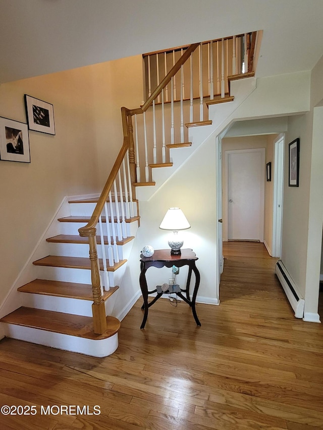staircase featuring baseboards, a baseboard heating unit, and wood finished floors