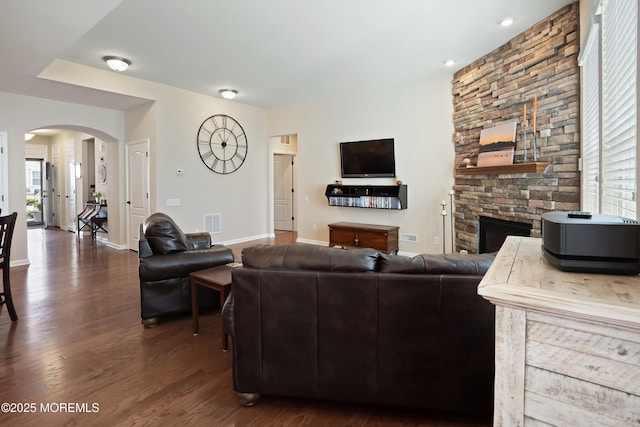 living room with baseboards, arched walkways, visible vents, a stone fireplace, and wood finished floors