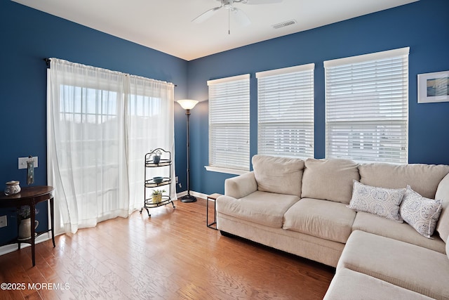living area featuring a ceiling fan, visible vents, baseboards, and wood finished floors