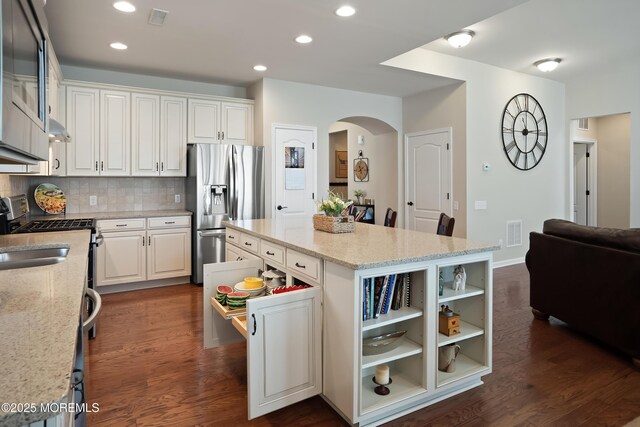 kitchen featuring tasteful backsplash, a center island, stainless steel appliances, visible vents, and arched walkways