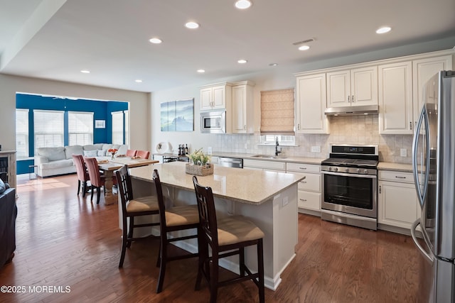 kitchen with a sink, open floor plan, under cabinet range hood, stainless steel appliances, and visible vents