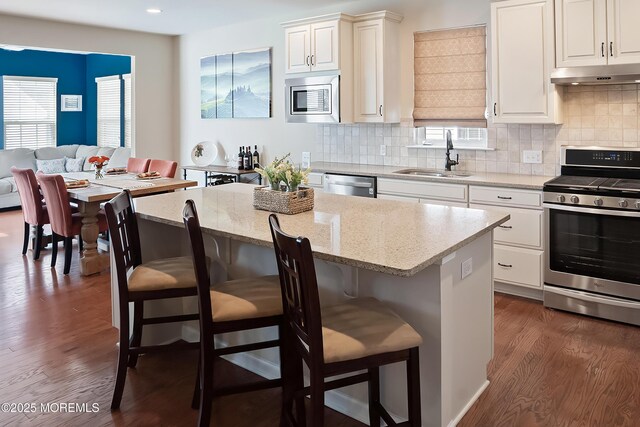 kitchen with a kitchen breakfast bar, a sink, stainless steel appliances, and under cabinet range hood