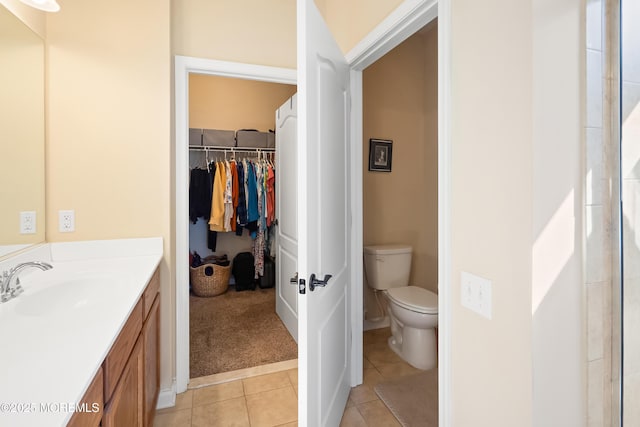 bathroom with tile patterned floors, a walk in closet, toilet, and vanity