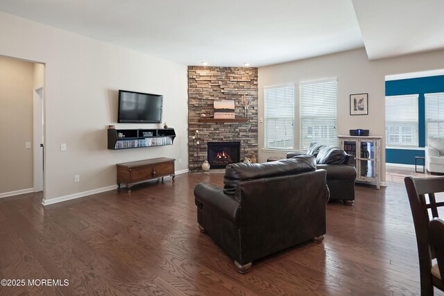 living area with a stone fireplace, dark wood-style floors, baseboards, and plenty of natural light