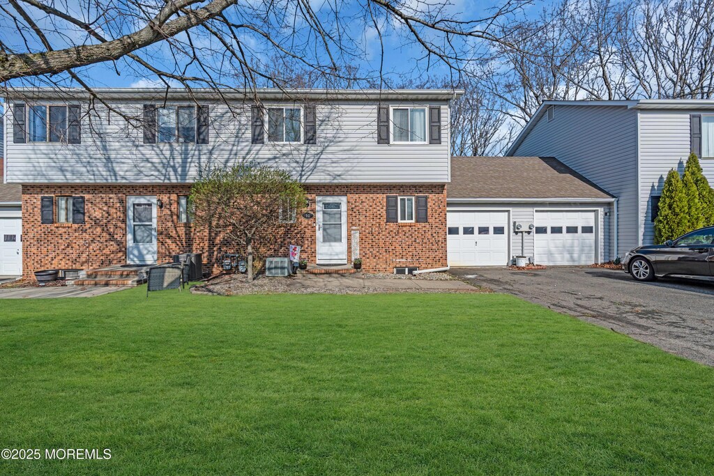 colonial inspired home featuring an attached garage, driveway, a front lawn, and brick siding