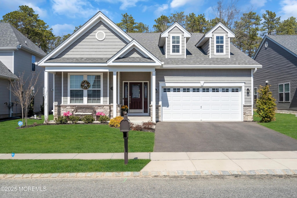 view of front facade with stone siding, a garage, a shingled roof, a front yard, and aphalt driveway