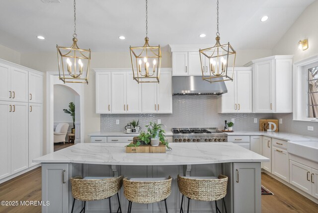 61 Windermere Rd, Lincroft, NJ 07738 - kitchen featuring a center island, under cabinet range hood, arched walkways, white cabinets, and a notable chandelier