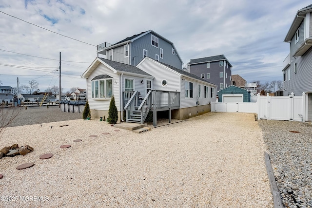 rear view of property featuring a gate, fence, a wooden deck, a garage, and driveway