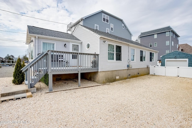 rear view of property featuring fence, a wooden deck, crawl space, roof with shingles, and an outdoor structure