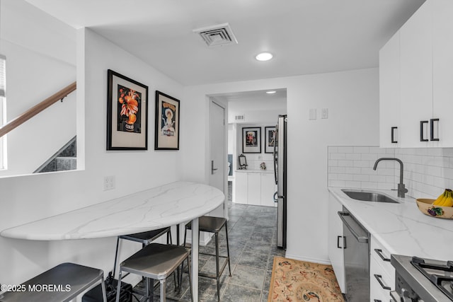 kitchen with a sink, stainless steel appliances, visible vents, white cabinets, and decorative backsplash