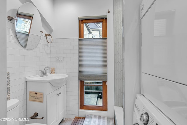 bathroom with a shower, vanity, tile walls, toilet, and stacked washing maching and dryer