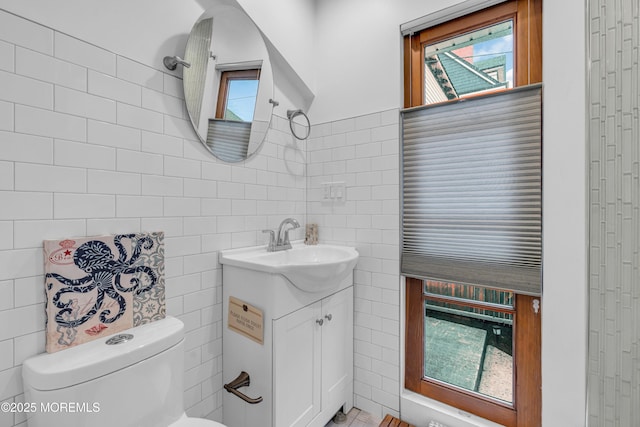 bathroom with toilet, vanity, tile walls, and a healthy amount of sunlight