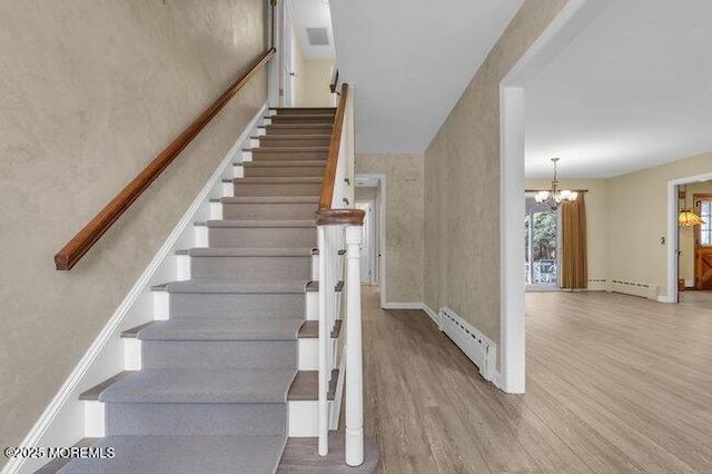 stairs featuring a notable chandelier, baseboards, a baseboard heating unit, and wood finished floors