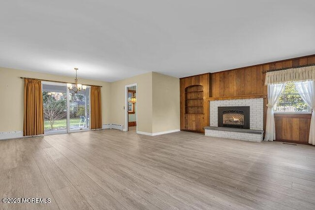 unfurnished living room featuring light wood finished floors, a wealth of natural light, built in shelves, and a chandelier