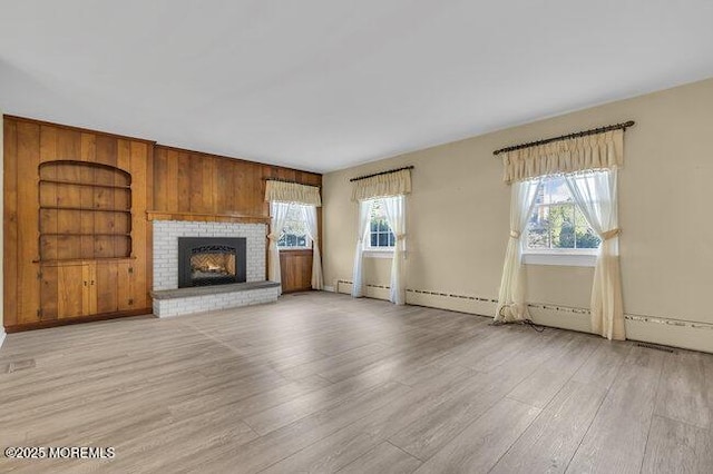 unfurnished living room featuring built in features, a fireplace, a healthy amount of sunlight, and light wood finished floors