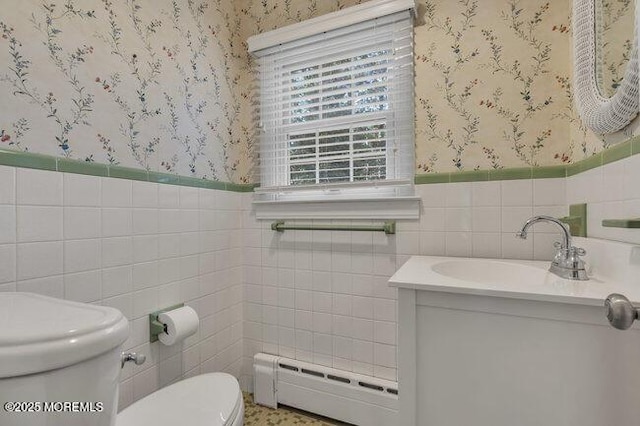 half bath featuring vanity, a baseboard heating unit, toilet, wallpapered walls, and a wainscoted wall