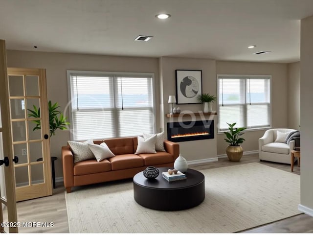 living area with a glass covered fireplace, visible vents, light wood-type flooring, and baseboards