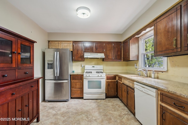 kitchen with white appliances, under cabinet range hood, a sink, light stone counters, and light tile patterned floors