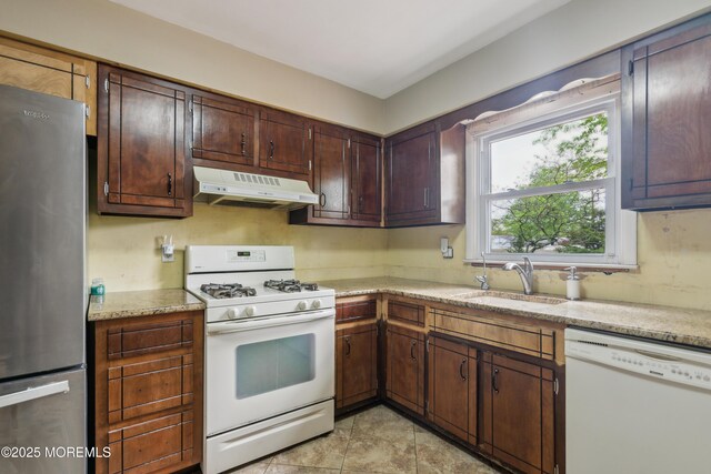 kitchen with white appliances, under cabinet range hood, a sink, dark brown cabinetry, and light tile patterned floors