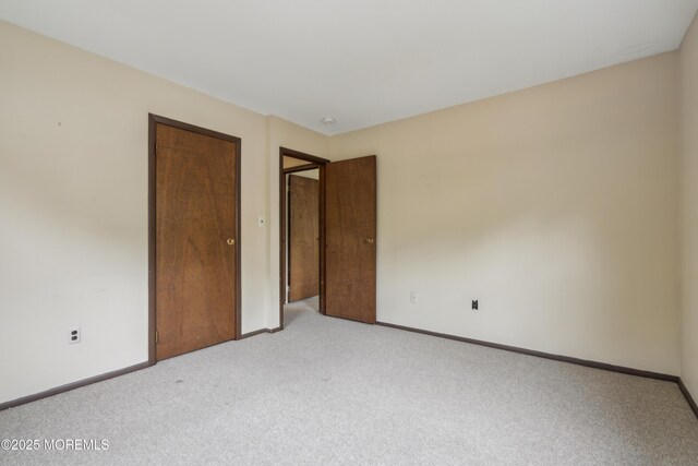 unfurnished bedroom with light colored carpet, a closet, and baseboards