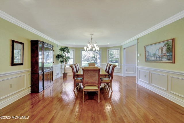 dining area featuring an inviting chandelier, crown molding, light wood-style floors, and a decorative wall