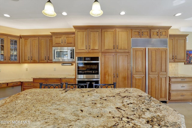 kitchen featuring light stone countertops, built in appliances, brown cabinets, and hanging light fixtures